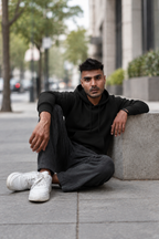 Original model का black hoodie में street seated pose