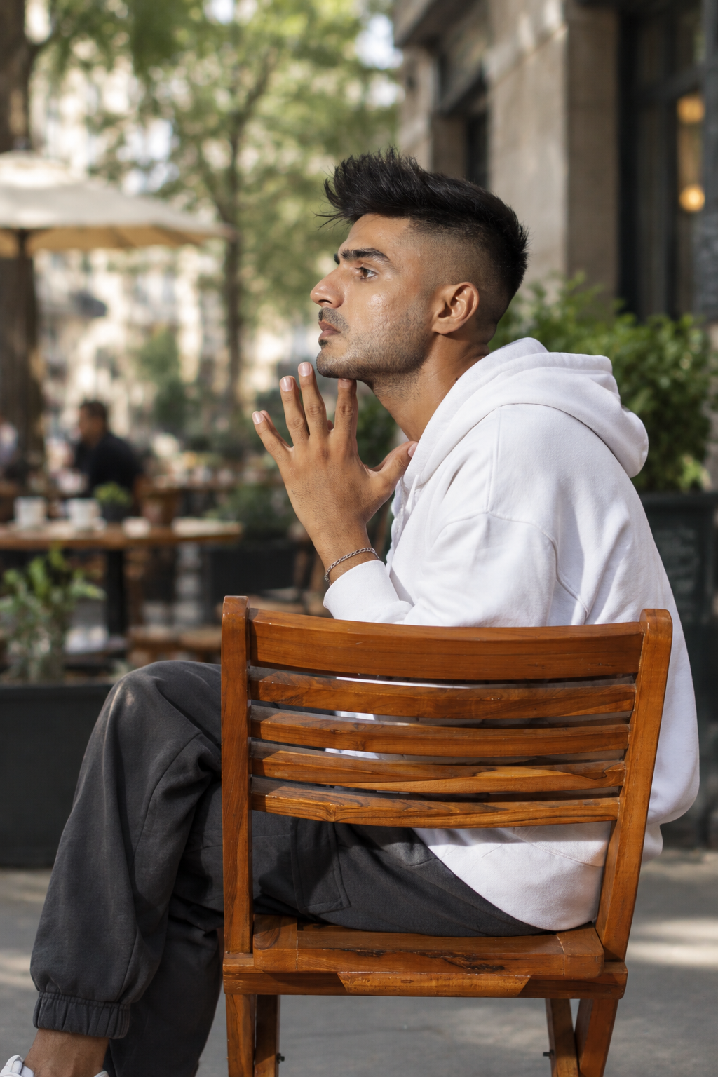 White hoodie में chair pose और textured hairstyle